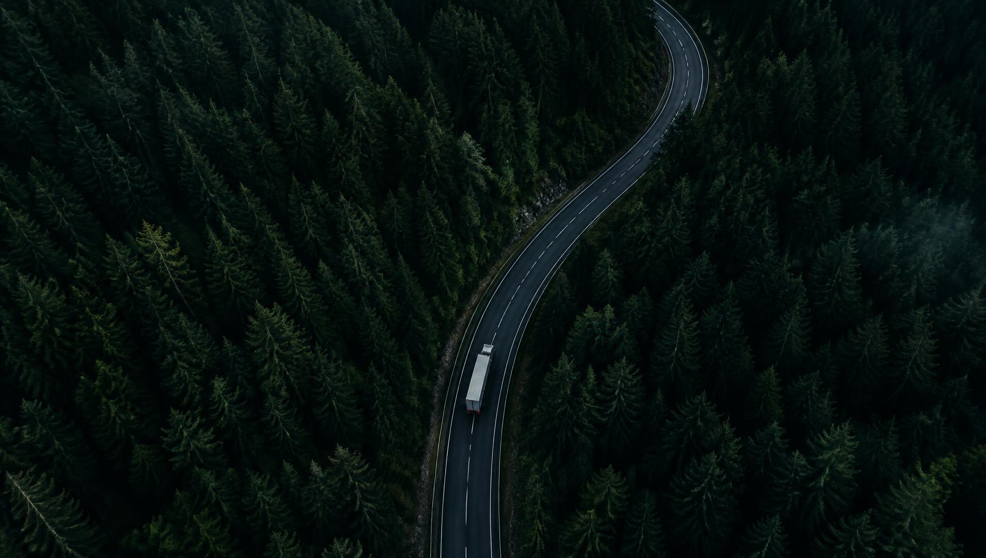 Vista aérea de uma estrada cortando uma floresta com um caminhão